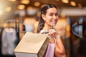 Portrait of a young mixed race woman smiling while holding shopping bags over her shoulder during a shopping spree in a mall. One hispanic female only enjoying retail therapy