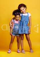 Studio portrait two mixed race girl sisters wearing funky sunglasses Isolated against a yellow background. Cute hispanic children posing inside. Happy and carefree kids imagining being fashion models