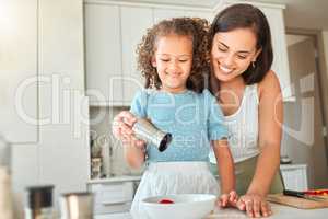 Happy mother teaching little daughter to cook in kitchen at home. Little girl adding seasoning to a bowl while making a salad with mom