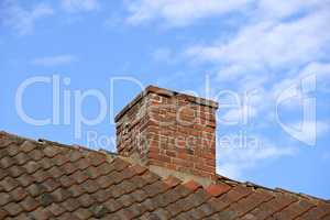 Red brick chimney designed on slate roof of a house building outside with blue sky background and copyspace. Exterior construction architecture of escape chute on rooftop for fireplace smoke and heat