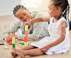 African american girl playing with building blocks while sitting with mother. Little girl building tower with wooden blocks. Smiling woman lying on the floor and playing with child