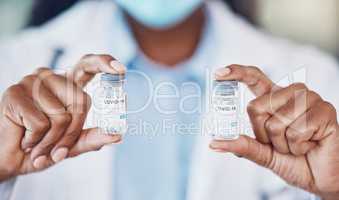 Closeup hand of african american woman doctor holding two bottles of the corona virus vaccine while standing in her hospital office. Be safe during the pandemic outbreak. Stop the spread of covid 19