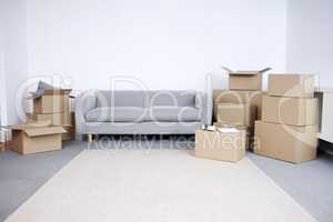 Lets get moving. Shot of cardboard boxes and a sofa in an empty living room during the day.