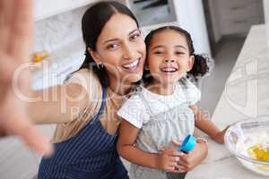 Happy mother and daughter baking and taking a selfie. Young woman teaching her daughter how to bake with a bowl of batter in the kitchen at home. Smiling mother cooking with her cute little girl
