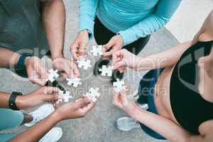 Closeup of diverse group of people from above assembling jigsaw puzzle pieces together. Hands of multiracial people working in synergy to problem solve. Using dedicated teamwork to support and help find common solutions