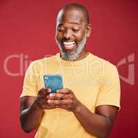 One happy African American man standing against a red studio background, holding and using his cellphone to browse the internet. Smiling black man laughing while browsing his phone for social media