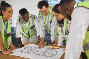 Closeup of a happy diverse multiracial group of architect colleagues analyzing a blueprint design on a building and discussing plans for the next project. Team of young and senior designers working on a strategy for a building construction plan while wear