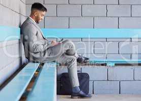 Staying mobile during his morning commute. a young businessman using a cellphone while sitting on a bench at a railway station during his commute.