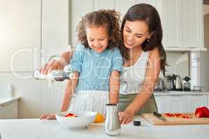 Happy mixed race mother and little daughter cooking together in the kitchen. Woman adding salad dressing while preparing a vegetarian meal with her child