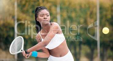 Young girl waiting to hit a ball in a tennis match. African american woman enjoying a game of tennis. Serious young woman playing tennis on her club court. Active, fit player hitting a tennis ball