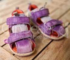 Top view of purple baby shoes on a table at home from above. Little girl footwear symbolizing new life, beginnings and pregnancy. Small stylish and fashionable sandals of a playful child on a desk