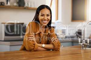Young cheerful beautiful mixed race woman enjoying a relaxing day alone at home. Confident hispanic female in her 20s smiling while relaxing in the kitchen at home
