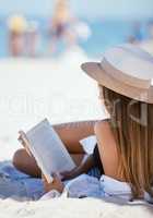 One beautiful young caucasian woman relaxing on the beach. Enjoying a summer vacation or holiday outdoors during summer. Taking time off and getting away from it all. Reading alone on the sand outside