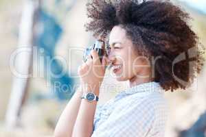 One young smiling mixed race woman with afro holding and using a camera to take photographs. Happy hispanic woman with curly hair taking pictures outside. Passionate and skilled in hobby photography
