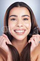 Close up portrait of a beautiful mixed race woman with clean skin and shiny smooth hair posing against a studio background. Woman holding her hair to show off healthy hair care