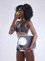 Im trying to lose a little extra weight. Studio shot of a woman holding an apple and a weight scale.