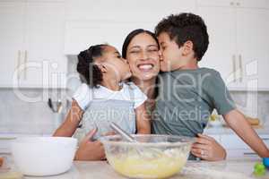 Happy mother baking with cute son and daughter bonding. A young woman teaching her children to bake at home. Smiling woman getting kisses and affection while cooking with her girl and boy at home