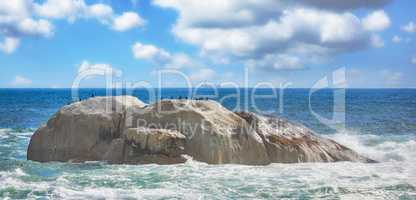 Scenic view of sea, rocks, and waves in Camps Bay Beach, Cape Town, South Africa. Tidal ocean with shoreline rocks and boulders. Overseas travel and tourism destination with blue sky and copy space
