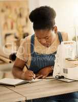 Creative designer planning notes in her notebook. Fashion designer writing a list. African American tailor writing in her notebook. Dressmaker working in her sewing studio
