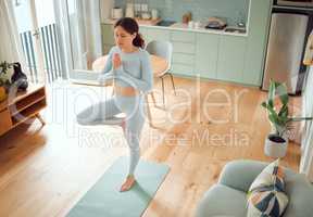 Beautiful young mixed race woman meditating while standing in an upright position while practicing yoga at home. Hispanic female exercising her body and mind, finding inner peace, balance and clarity