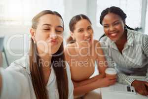 Portrait of a confident young hispanic business woman making a funny face expression while taking selfies with her colleagues in an office. Group of three happy smiling women taking photos as a dedicated and ambitious team in a creative startup agency