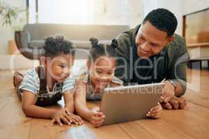 A happy mixed race family of three relaxing and lying on the lounge floor together. Loving black single parent bonding with his kids while using a digital tablet stream