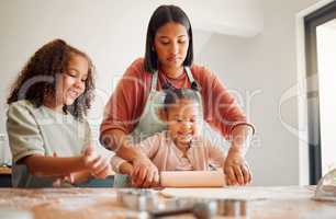 Females only, happy mixed race family of three cooking in a messy kitchen together. Loving black single parent bonding with her daughters while teaching them domestic skills at home