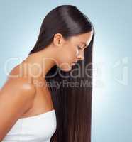 A hispanic brunette woman with long lush beautiful hair posing and looking serious against a grey studio background. Mixed race female standing showing her beautiful healthy hair