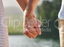 Hold tightly. an unrecognizable couple holding hands while spending time at a lake.