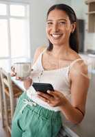Coffee and a good wi-fi connection is all you need. a woman holding her cellphone while drinking coffee at home.
