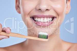 Closeup of a smiling mixed race young woman with glowing skin posing against blue copyspace background while brushing her teeth for fresh breath. Hispanic model using toothpaste to prevent a cavity