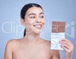 A beautiful mixed race woman holding a slab of chocolate. Hispanic model snacking on dessert against a blue copyspace background