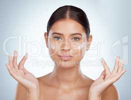 Portrait beautiful woman applying face cream while posing with copyspace. Caucasian model isolated against grey studio background with product on cheek. Moisturise and sunscreen for healthy skincare