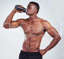 One young African American fitness model posing topless while drinking water from a bottle .Confident black male athlete isolated on grey copyspace is focused on staying hydrated while exercising