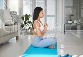 Push yourself mentally, physically and spiritually. a sporty young woman meditating while practising yoga at home.