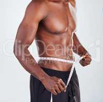 One unrecognizable African American fitness model posing topless with tape measure around his waist while looking muscular. Confident male athlete isolated on grey copyspace after positive weight loss