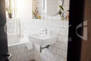 A clean and tidy bathroom inside a house. A basin, bath, with ceramic tiling and a round mirror hanging on the wall. A clean, hygienic, bright room