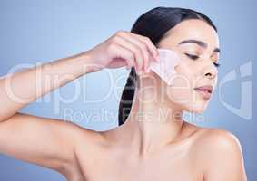 A beautiful mixed race woman using a rose quartz gua sha to reduce wrinkles and promote cell renewal. Young hispanic woman using anti ageing tool against blue copyspace background