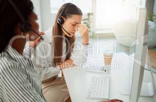 Stressed young hispanic call centre agent looking worried and suffering with headache while being comforted and consoled by a colleague in an office. Woman offering sympathy and support to frustrated and upset coworker