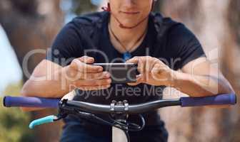 One athletic unrecognizable male using a cellphone while cycling outside on a bike for exercise. Sporty fit male taking a break to text, browse online and use navigation apps while standing outside