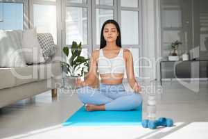 Focus on becoming the greatest version of yourself. a sporty young woman meditating while practising yoga at home.