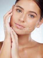 Closeup of beautiful woman with smooth glowing skin touching face in studio. Headshot of serious caucasian model isolated against grey background and showing manicured hand. Healthy self care routine