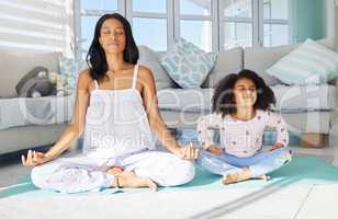 Focusing on finding peace. a young mother and daughter meditating together at home.