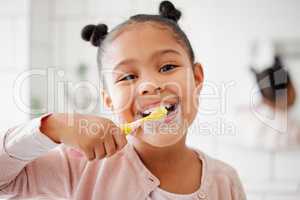 One mixed race adorable little girl brushing her teeth in a bathroom at home. A happy Hispanic child with healthy daily habits to prevent cavities and strengthen enamel