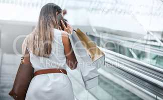 Rear view of a woman talking on her cellphone while out on a shopping spree. Female having retail therapy while staying connected with her smartphone. Calling to find a sale and discount. Telling friends about sale at mall or calling bank to increase spen