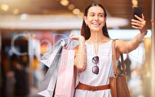 Happy young woman taking selfies on a cellphone during a shopping spree in a mall. One female only enjoying retail therapy while taking pictures. Happy shopaholic holding bags and making a video call