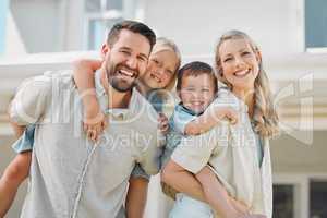 Portrait of happy parents giving their little children piggyback rides outside in a garden. Smiling caucasian couple bonding with their adorable son and daughter in the backyard. Playful kids enjoying