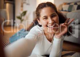 Cheerful woman taking a selfie at home. Young woman making the peace sign with her finger. Young girl relaxing taking a selfie. Comfortable woman resting and relaxing at home