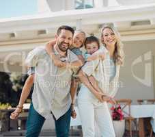 Portrait of happy parents giving their little children piggyback rides outside in a garden. Smiling caucasian couple bonding with their adorable son and daughter in the backyard. Playful kids enjoying