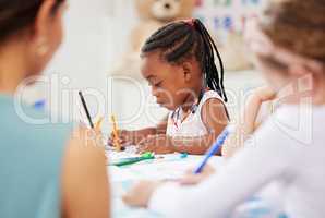 African american girl sitting at a table and colouring at pre-school or kindergarten with her fellow students. Young female child using colourful pencils to draw pictures in a classroom at her school